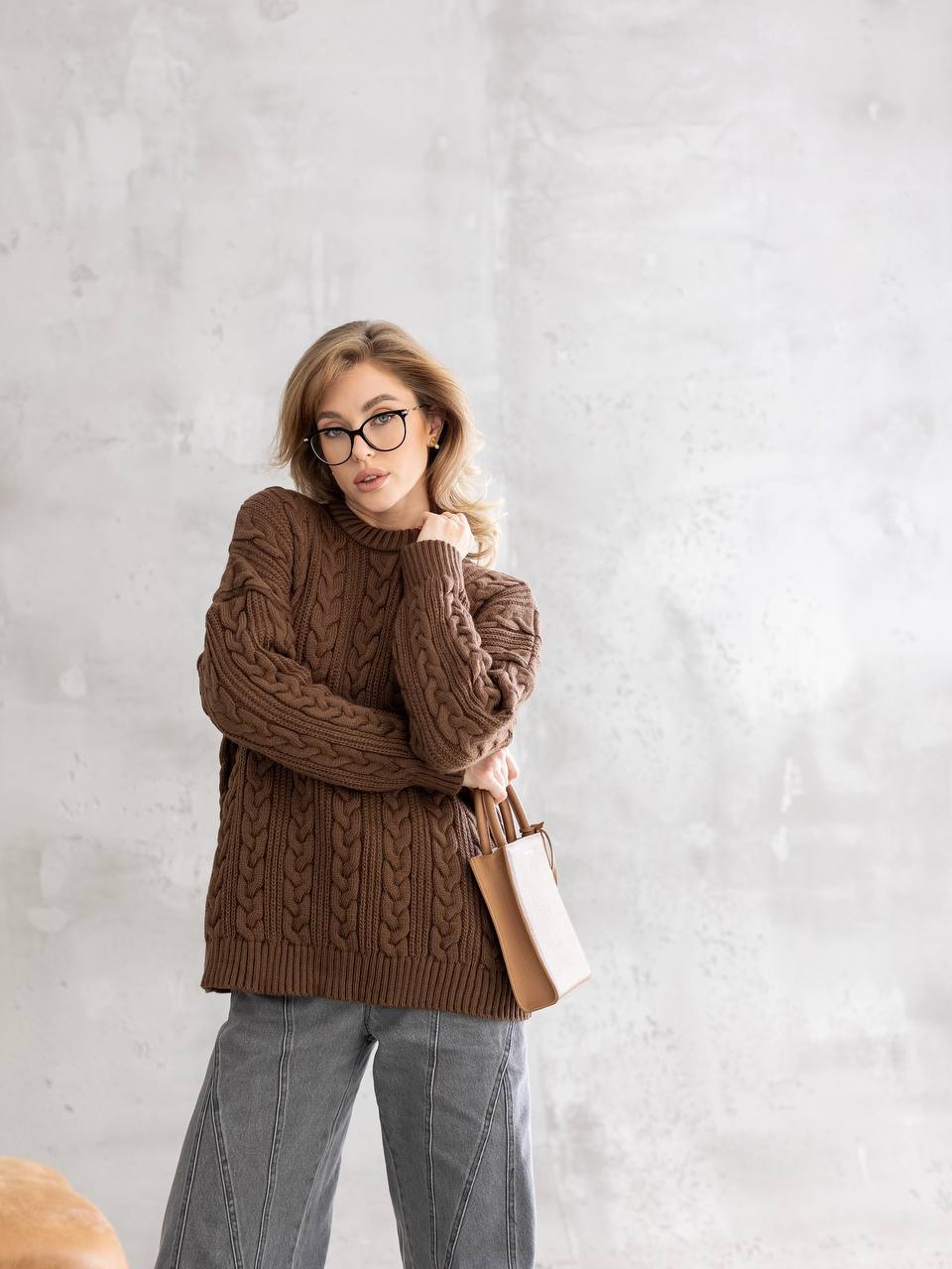 Woman wearing a brown cable knit sweater against a light gray background
