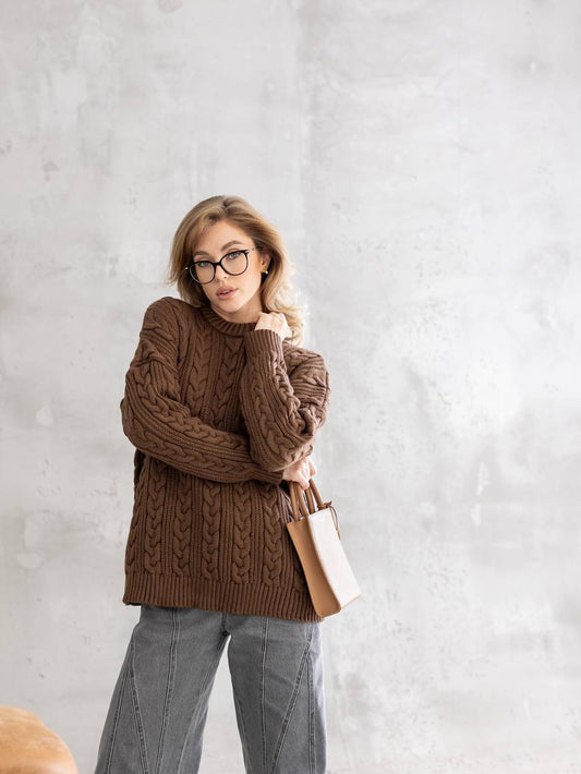 Woman wearing a brown cable knit sweater against a light gray background