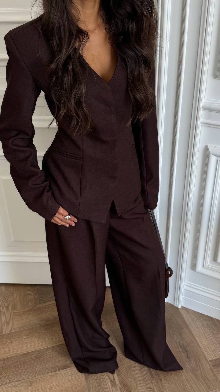Person wearing a brown suit standing in a room with wooden flooring and white walls.