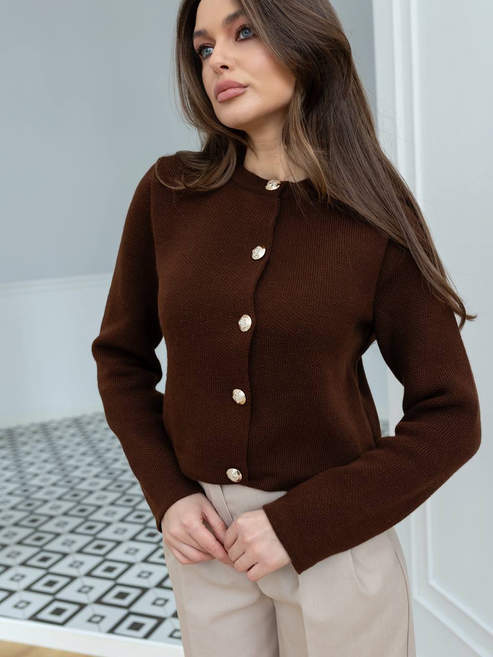 Woman wearing a brown cardigan with gold buttons indoors.