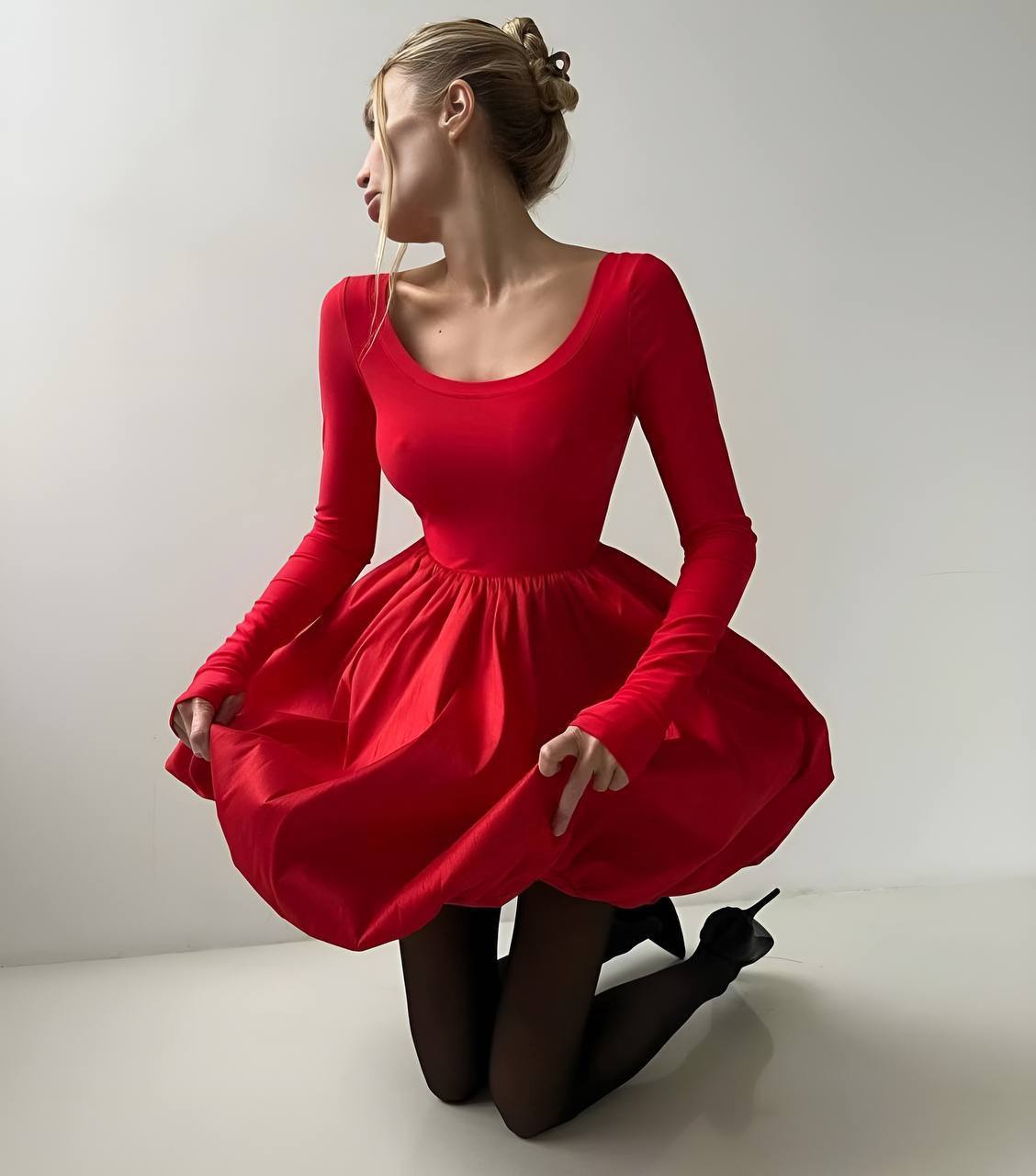 Woman wearing a red dress kneeling on a plain background