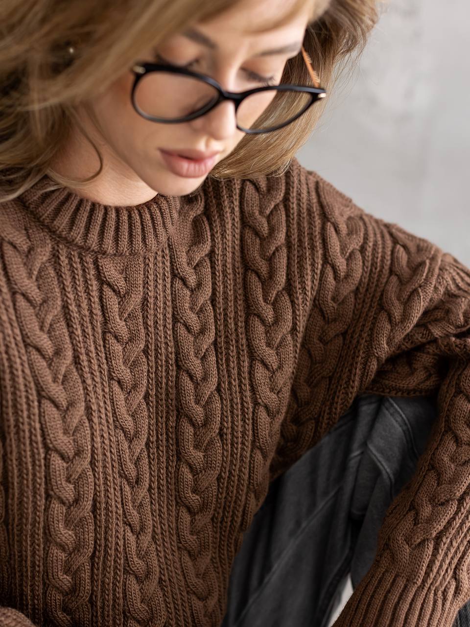 Person wearing a brown cable knit sweater with a neutral background