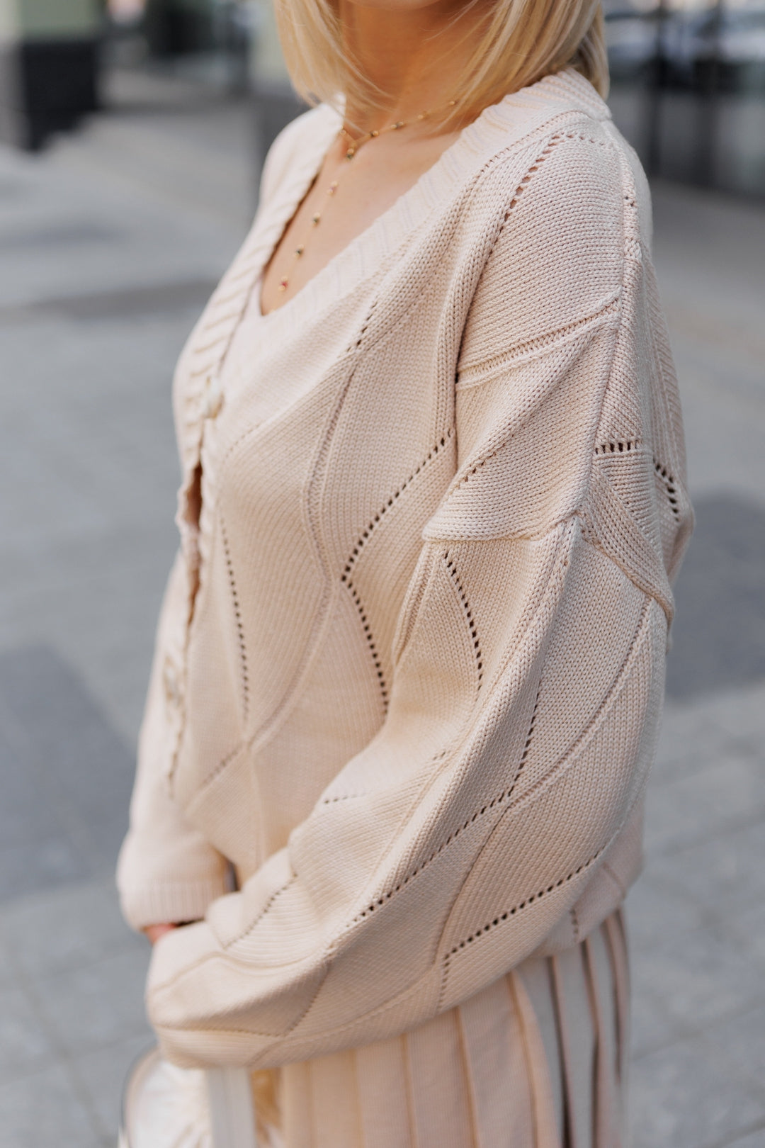 Person wearing a beige knitted cardigan in an urban setting