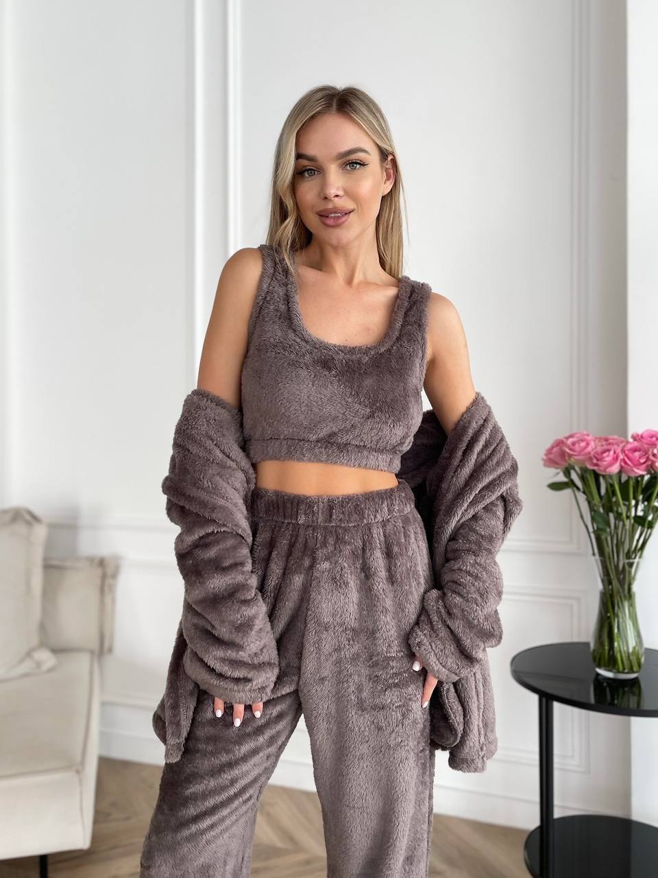 Woman wearing a brown outfit with a matching cardigan in a room with a vase of flowers.