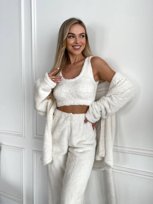 Woman wearing a white textured outfit with a matching cardigan against a white wall.