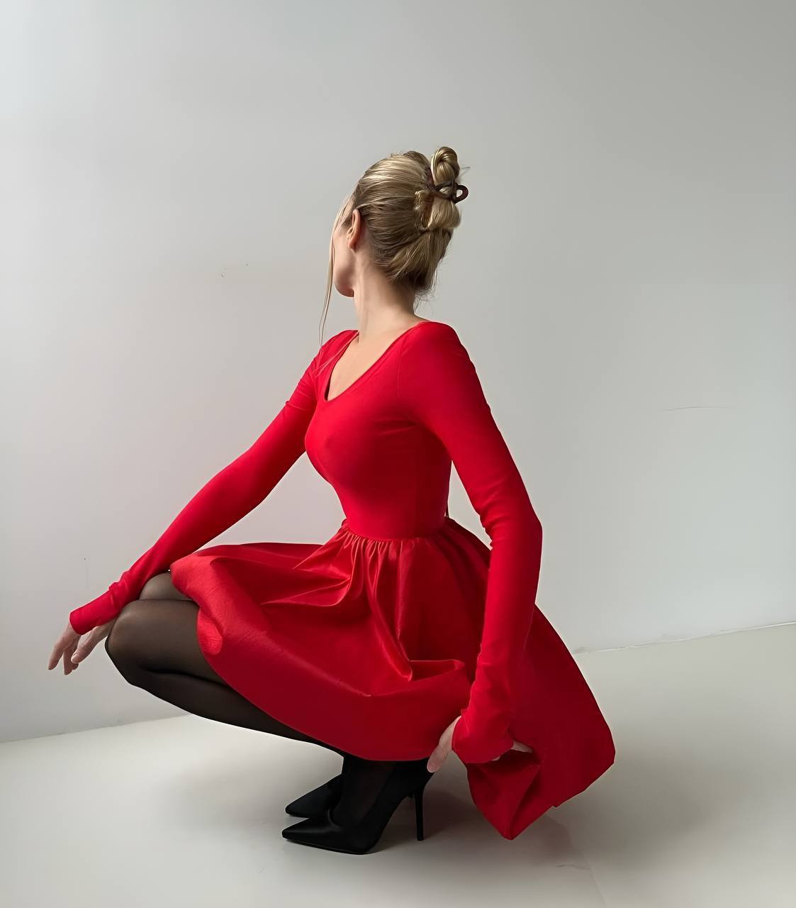 Woman in a red dress squatting on a plain background