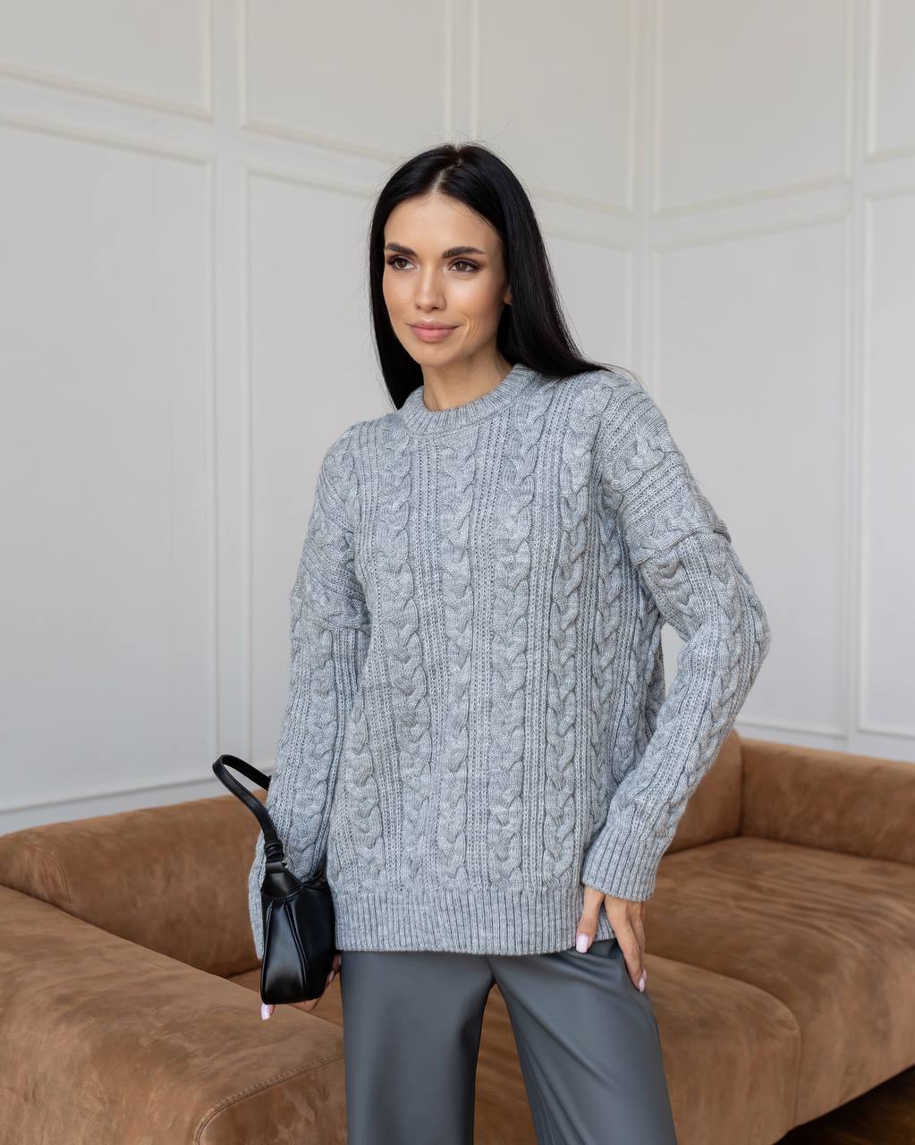 Woman wearing a gray cable knit sweater standing in front of a brown sofa.