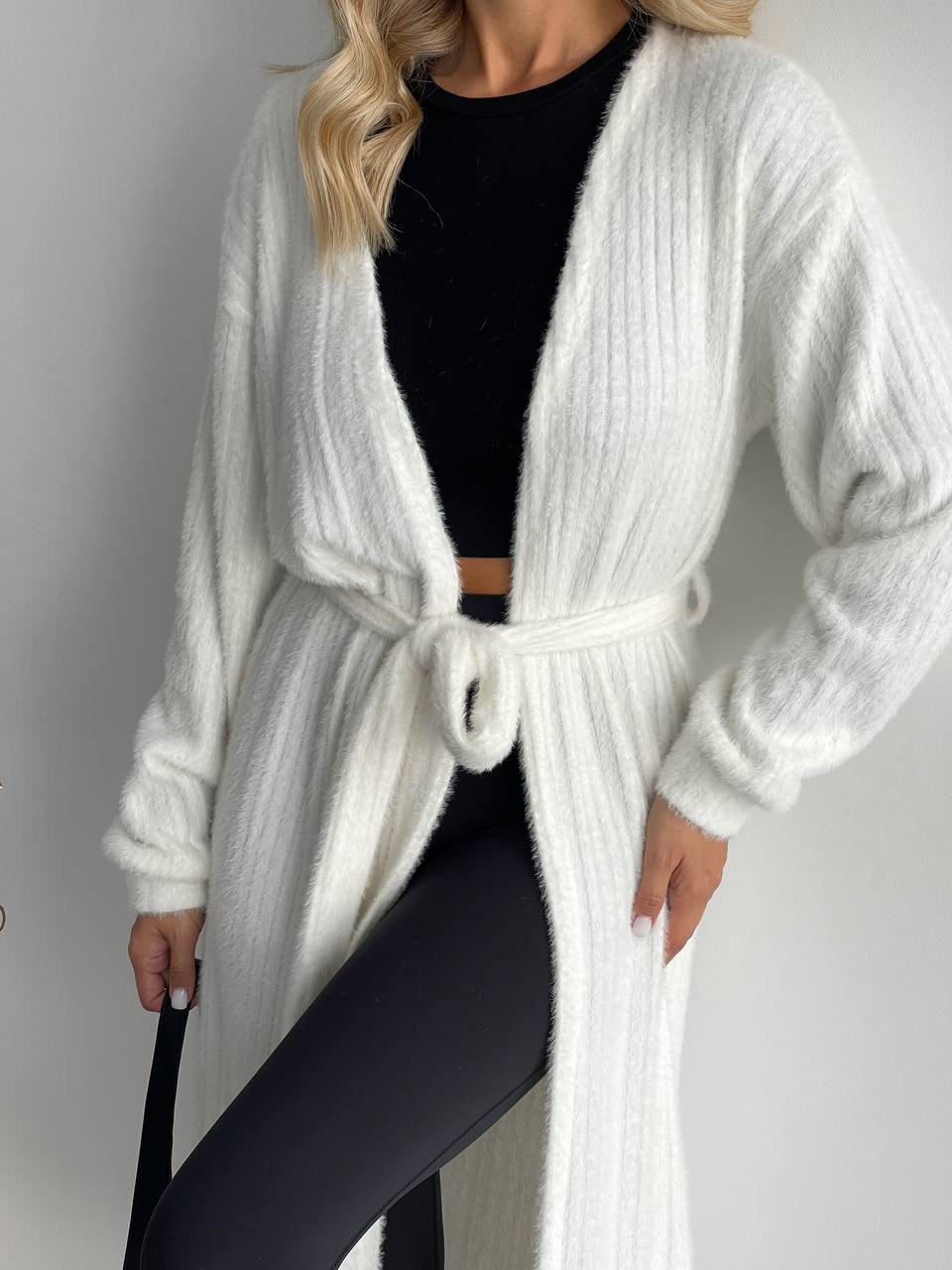 Person wearing a white knitted cardigan over a black outfit on a plain background