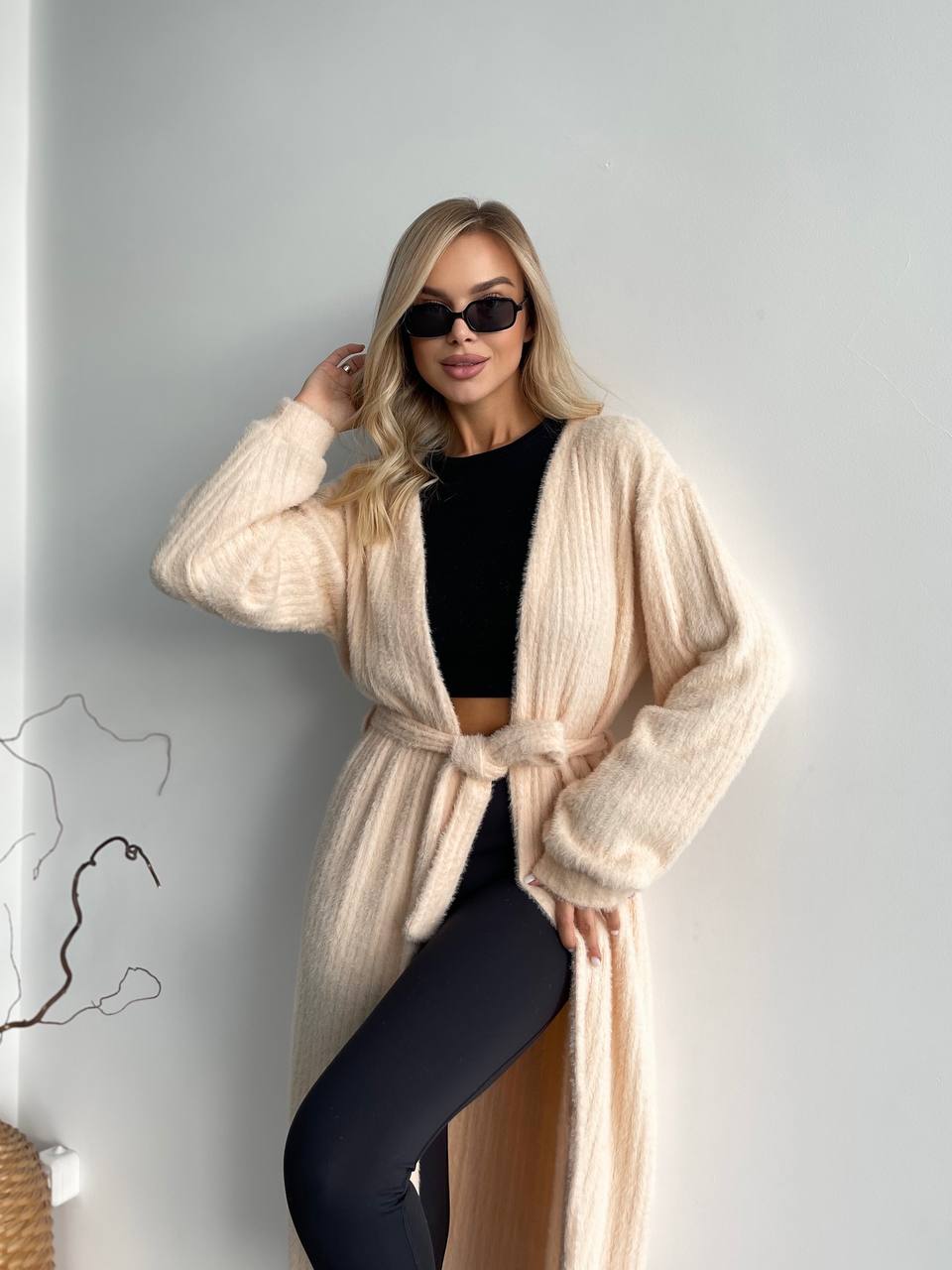 Woman wearing a beige cardigan over a black outfit against a plain background