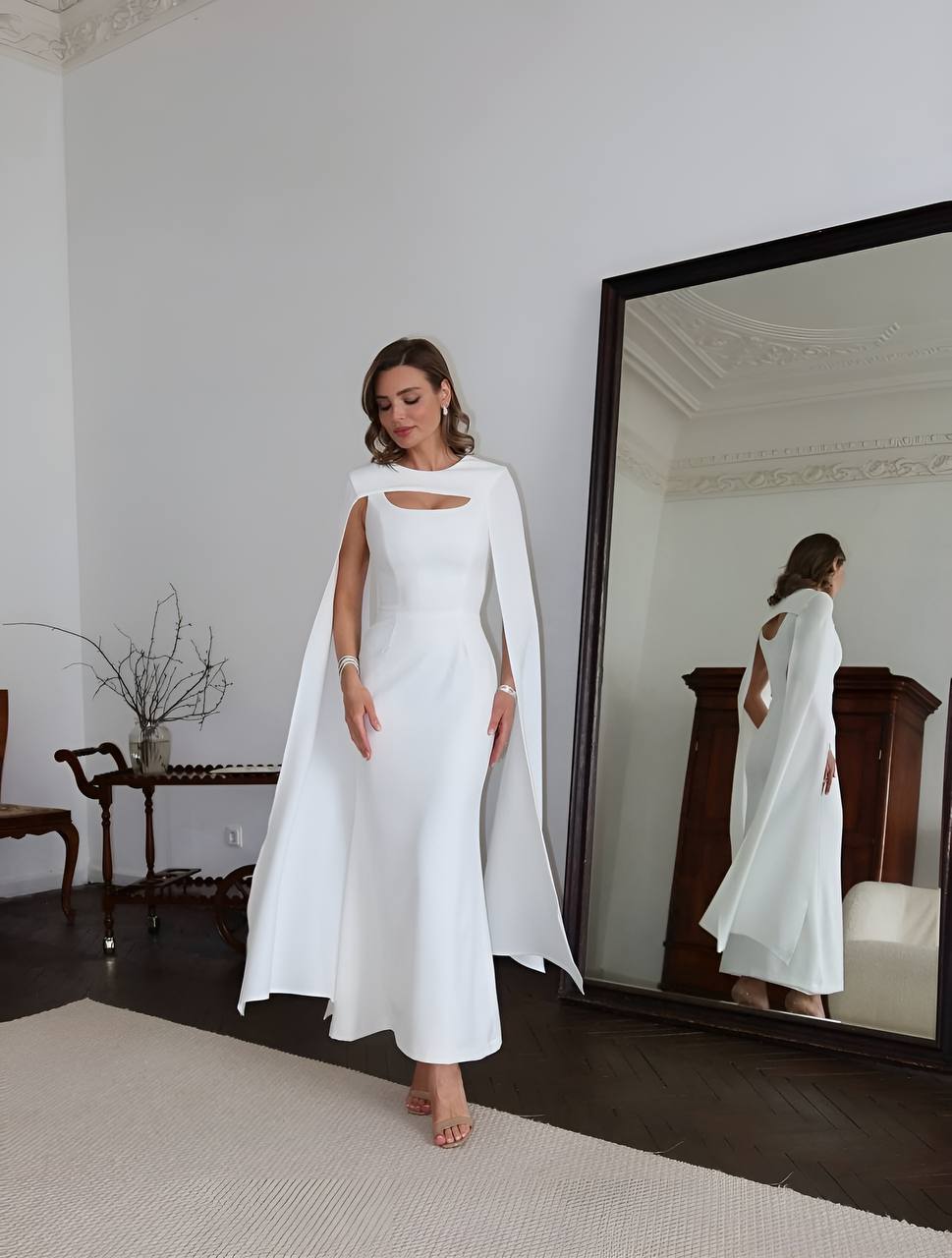 Woman in a white gown with a cape standing in front of a mirror.