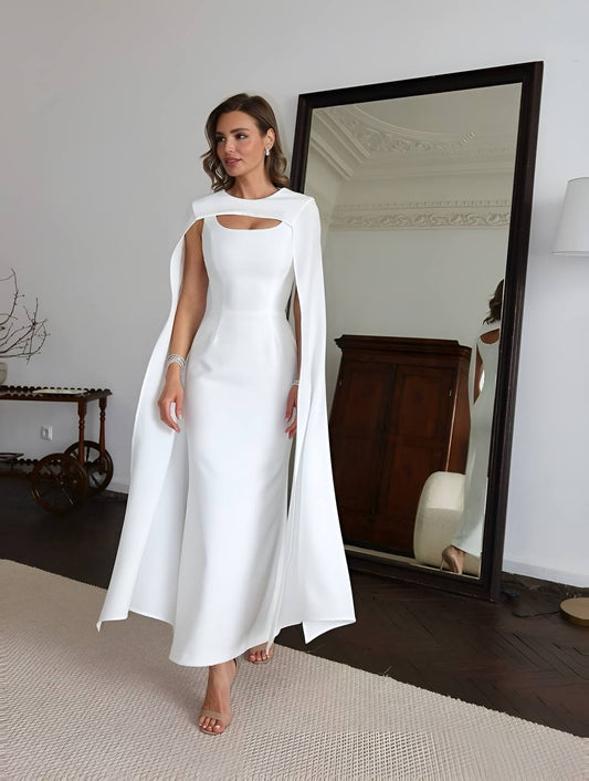 Woman wearing a white dress with a cape in a room with a large mirror.