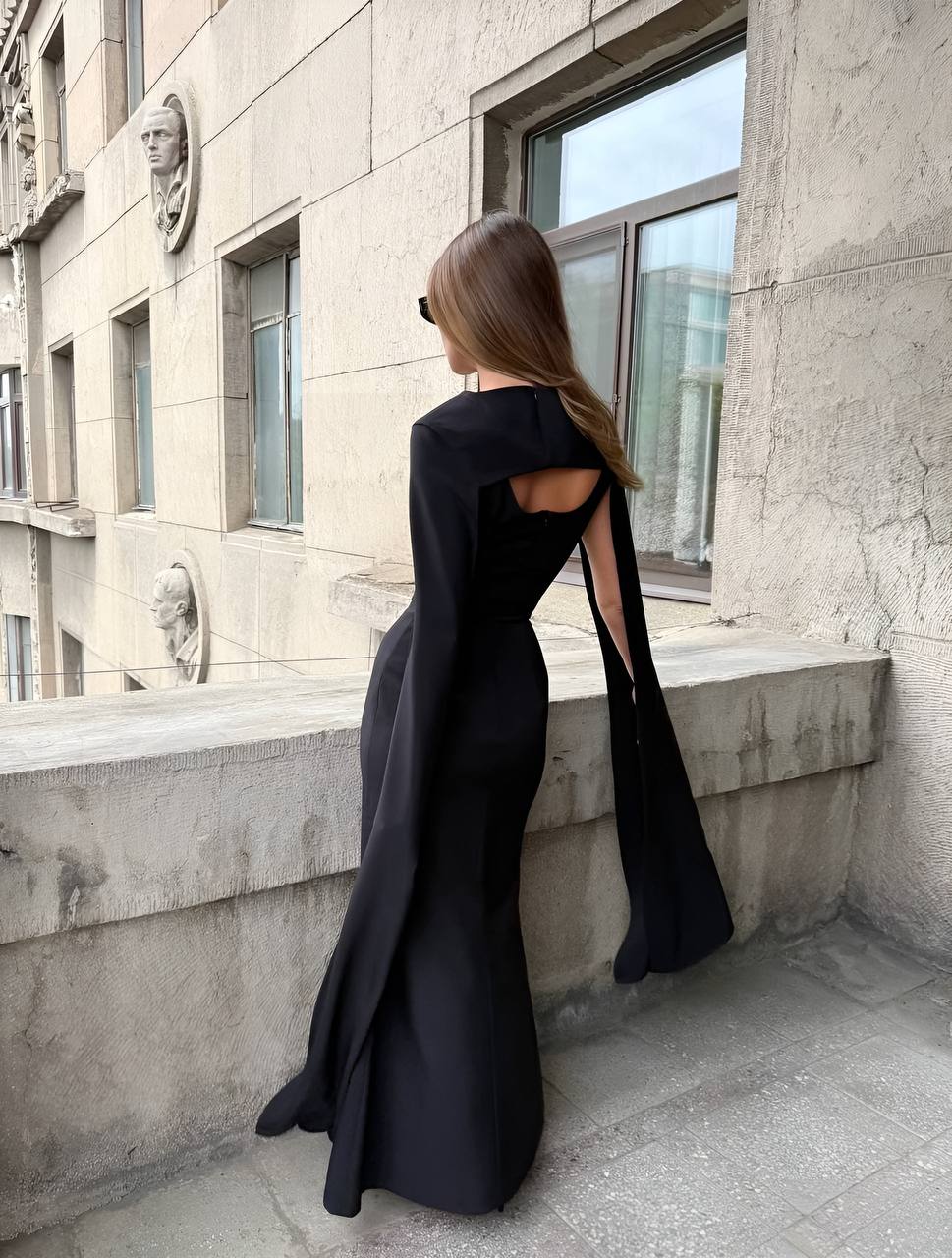 Woman in a black evening gown with cut-out design standing against a stone building.