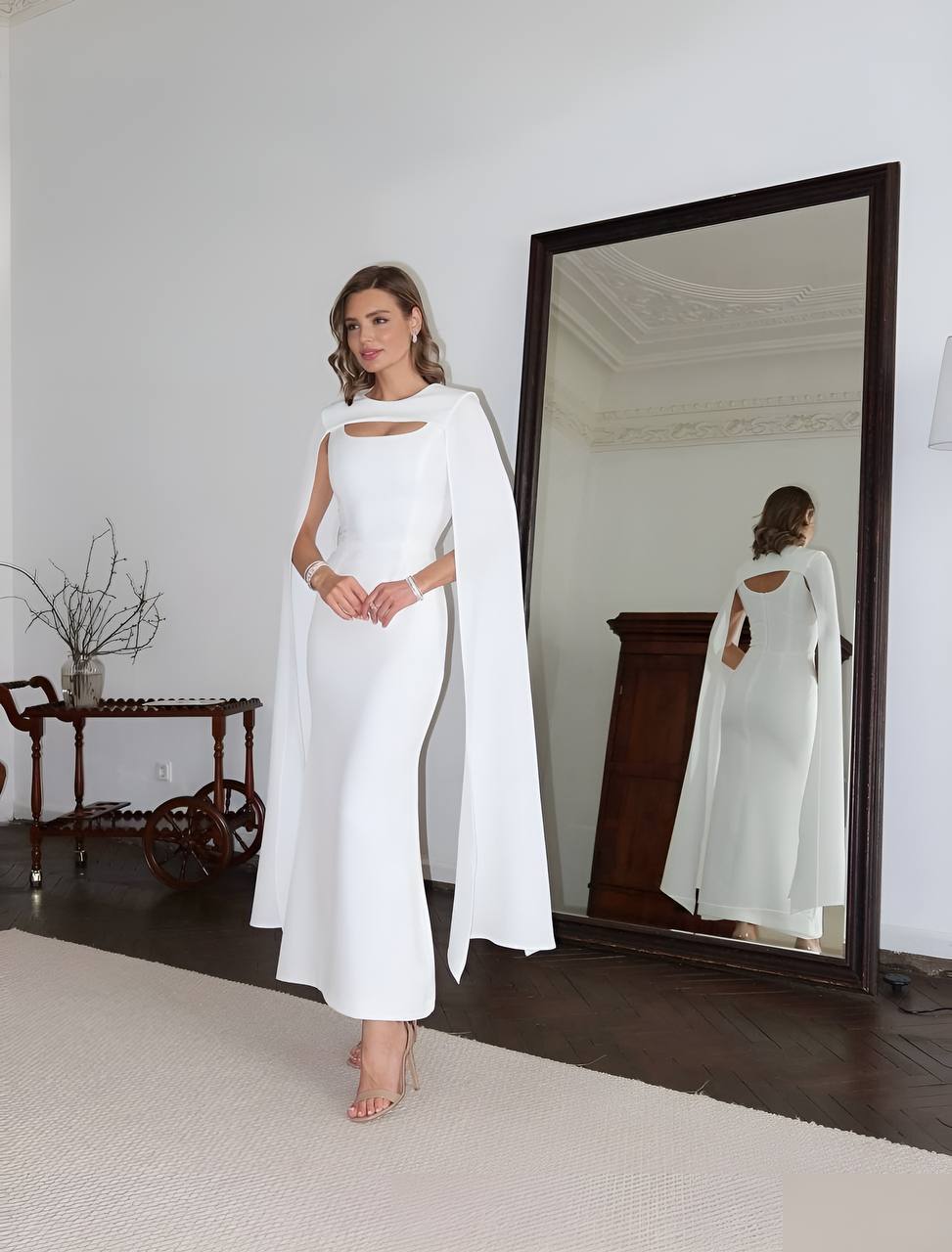 Woman in a white dress with a cape standing in front of a mirror.