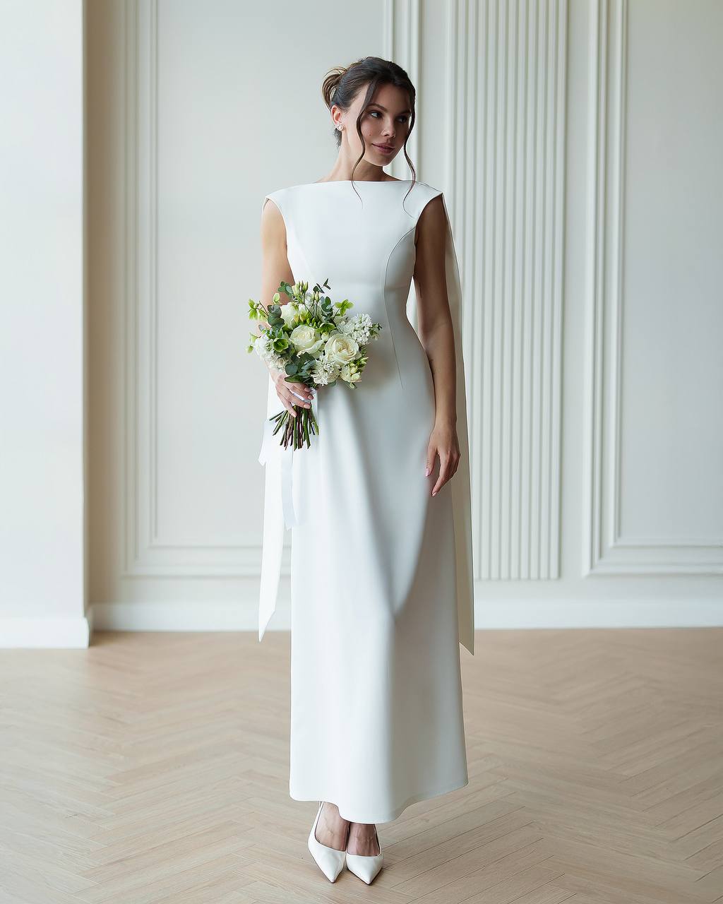 Woman in a white wedding dress holding a bouquet in a minimalistic setting