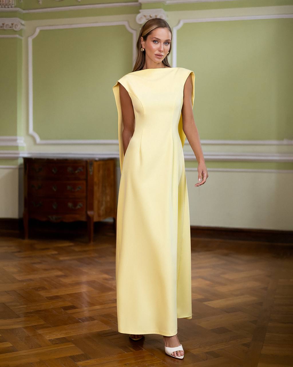 Woman wearing a yellow dress in an elegant room with green walls and wooden floor.