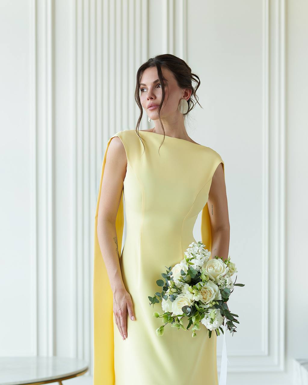 Woman in a yellow dress holding a bouquet against a white wall