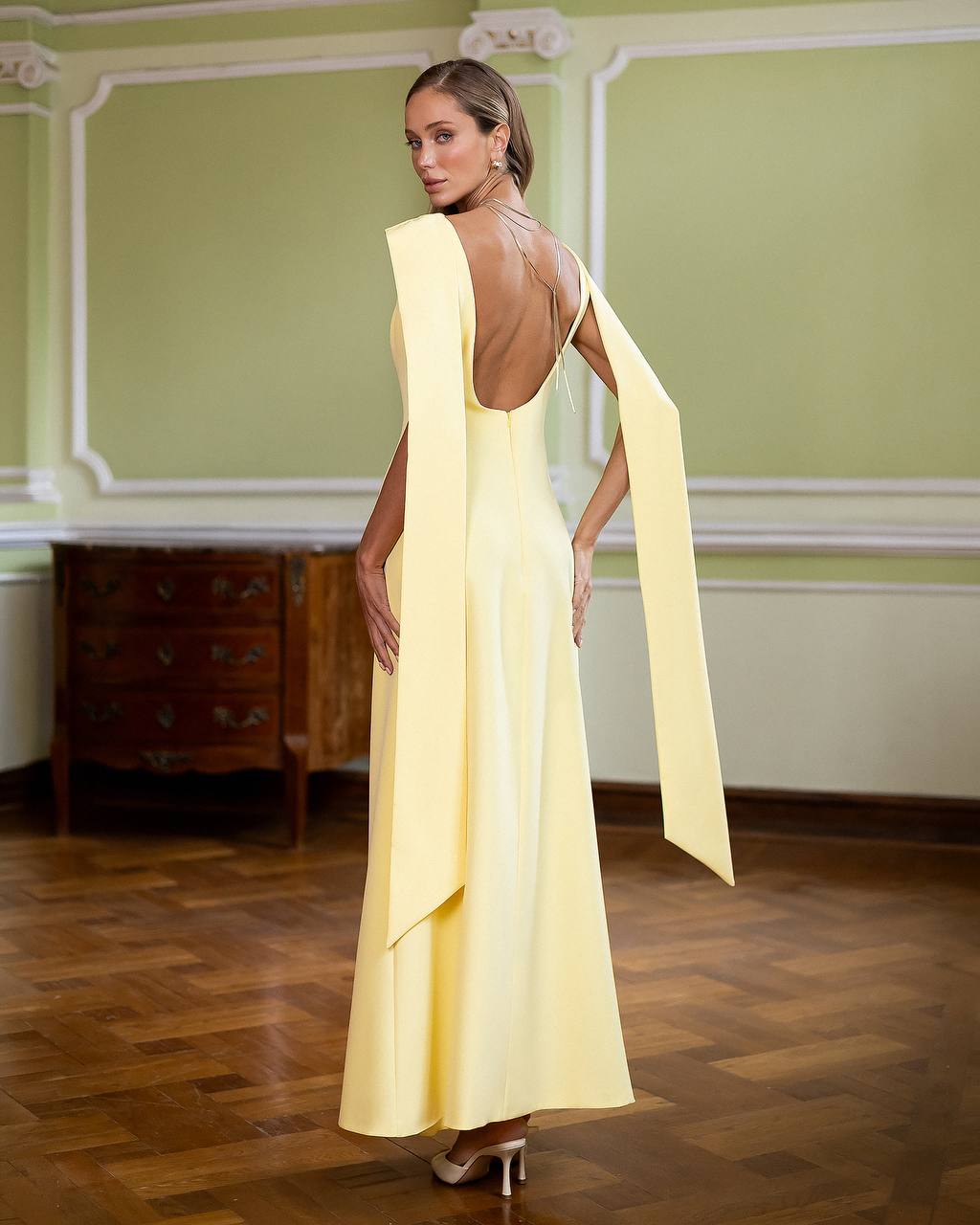 Woman wearing a yellow evening gown with a cape in an elegant room.