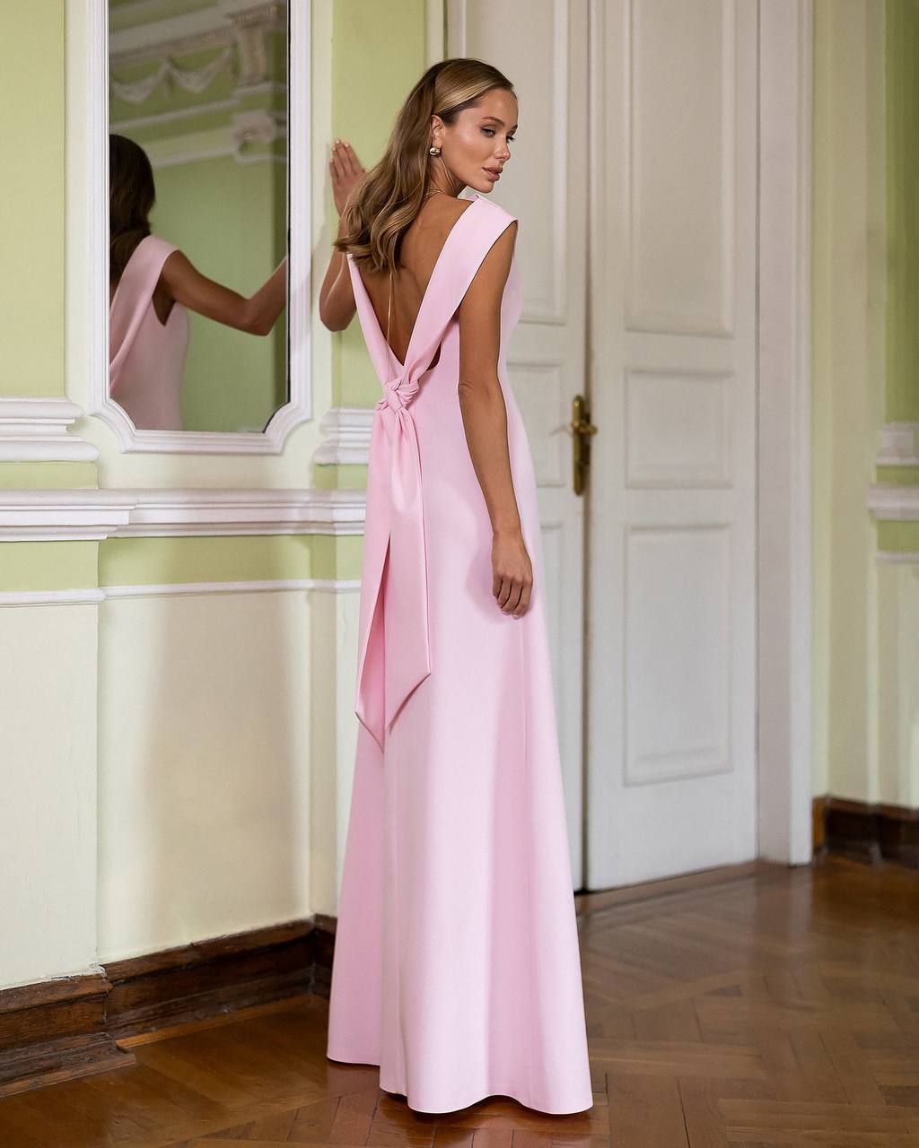 Woman in a pink evening gown standing in a room with a mirror.