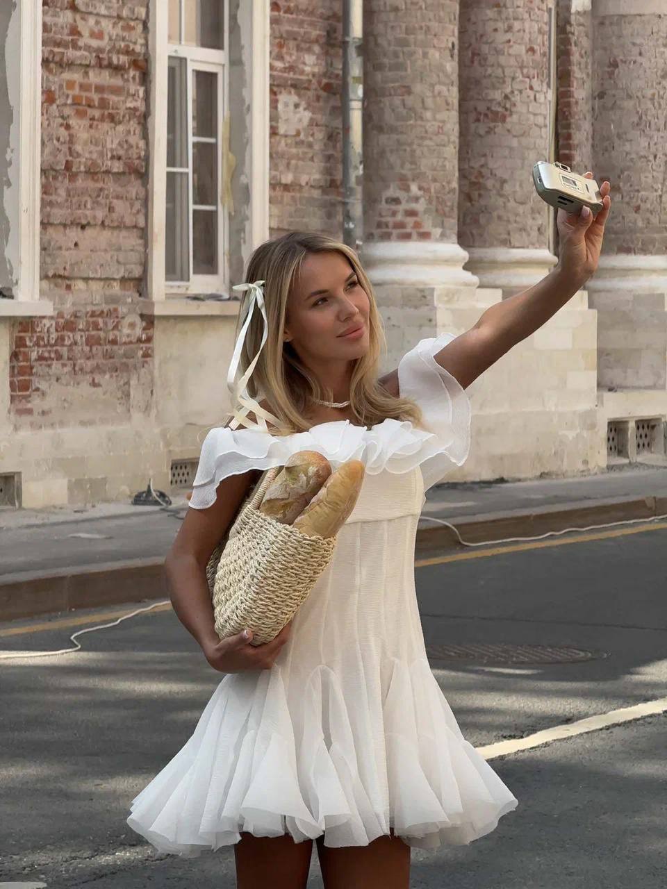 Woman in a white dress taking a selfie outdoors with classical architecture in the background