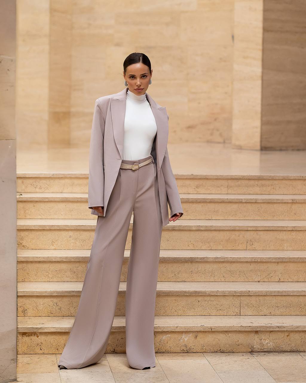 Woman in a gray suit standing on stone steps with a beige wall background