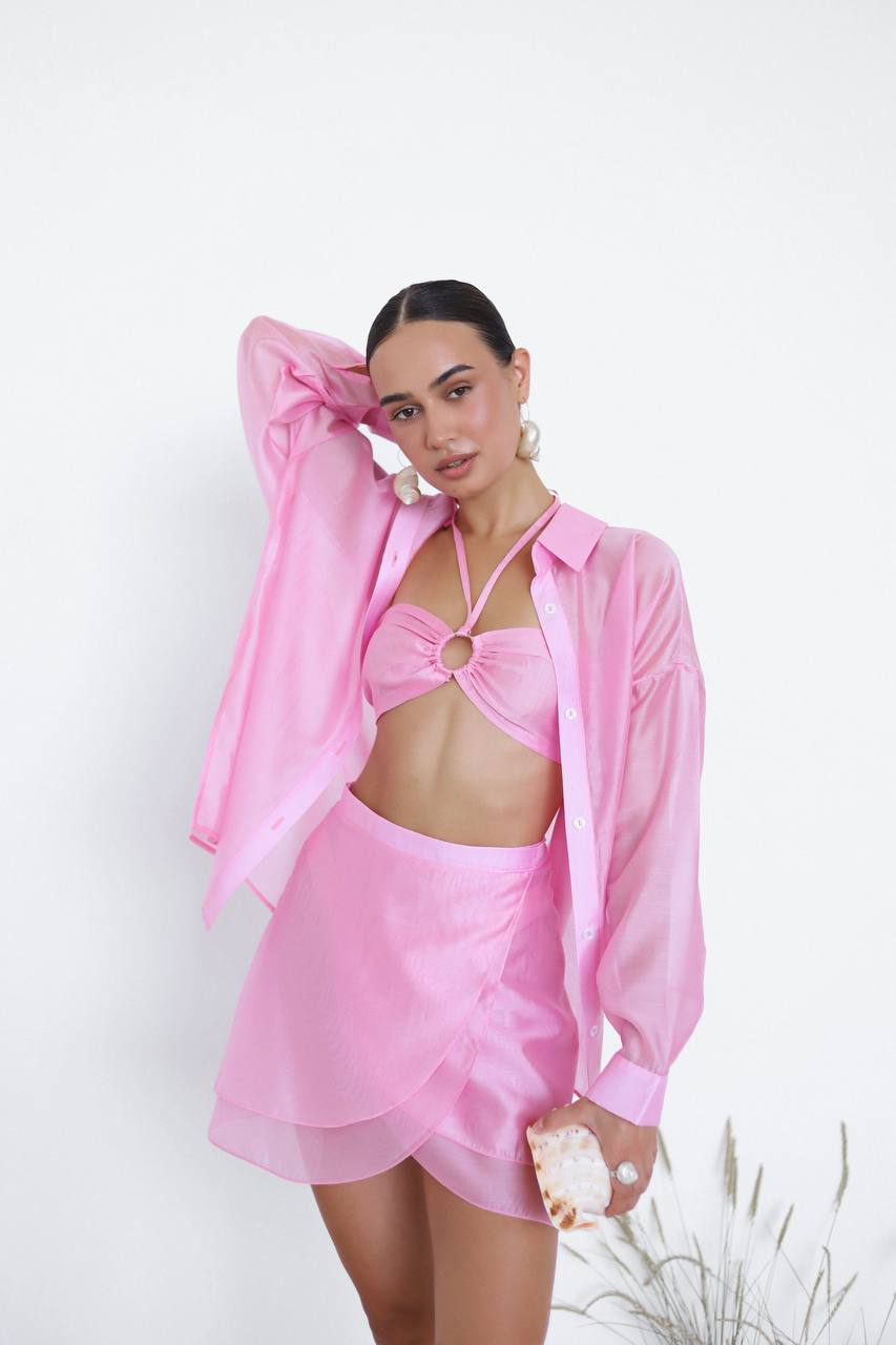 Woman wearing a pink outfit with a sheer cover-up against a white background