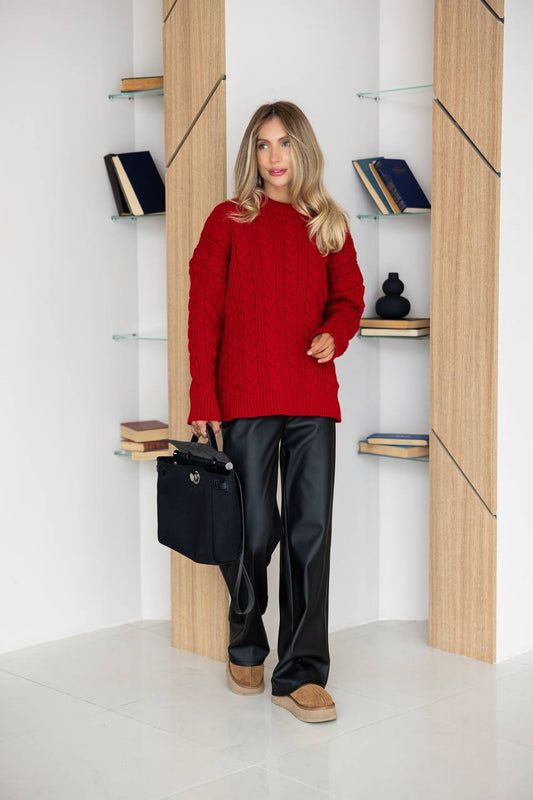 Woman in a red sweater and black pants standing in a room with wooden shelves.