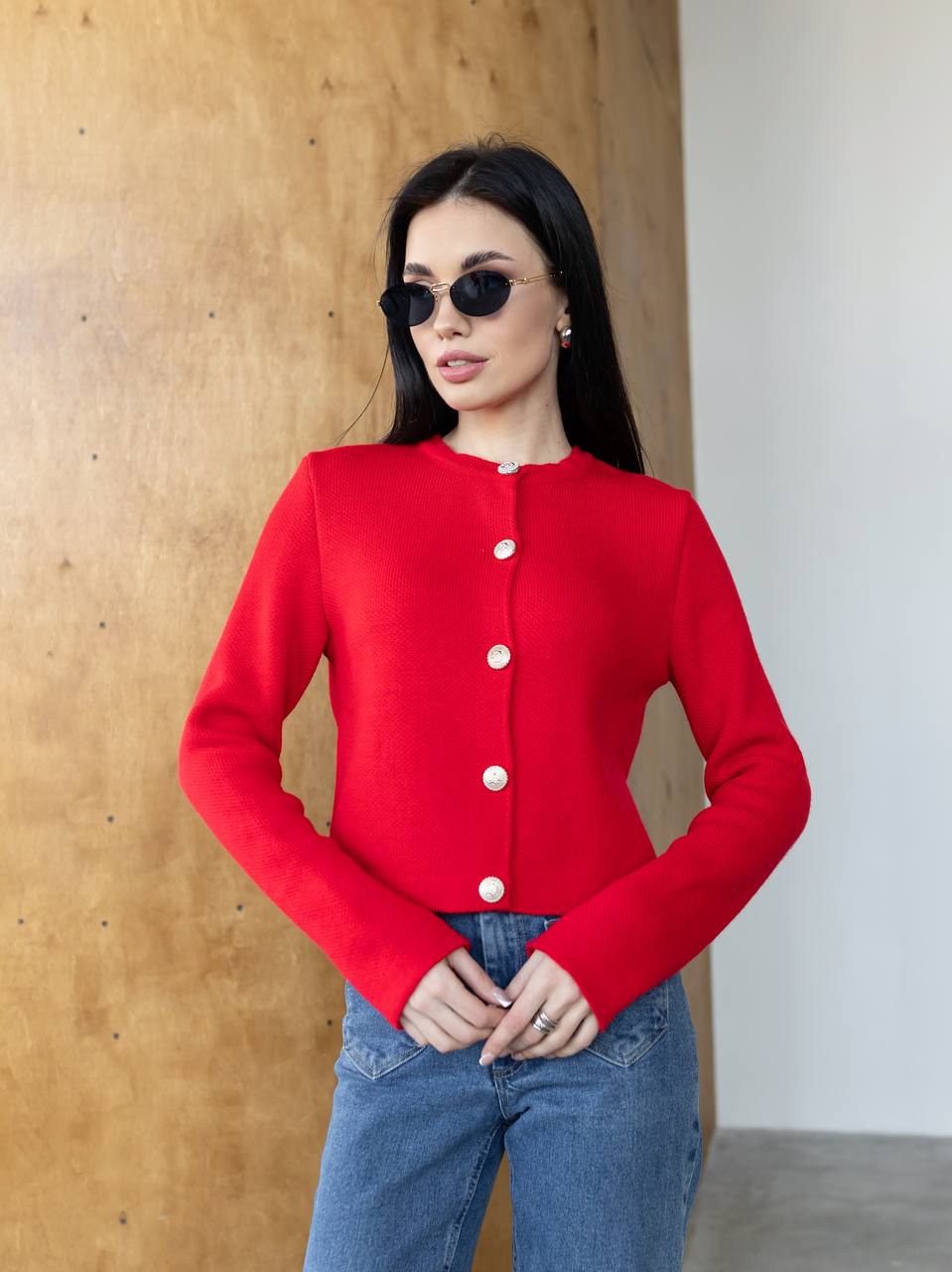 Woman wearing a red cardigan with white buttons against a wooden wall.