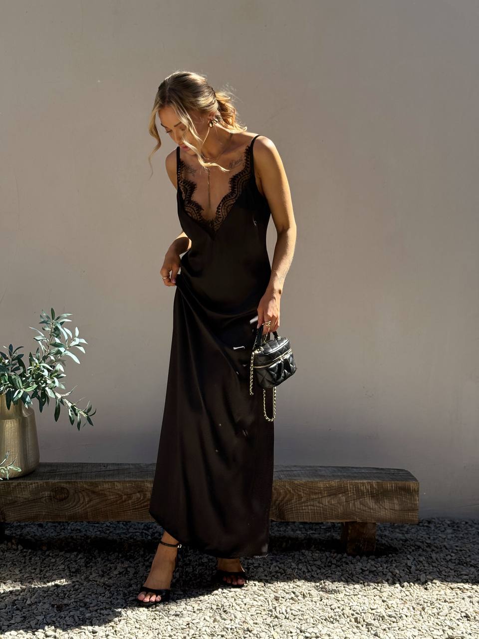 Woman in a black slip dress holding a handbag in a minimalistic setting.
