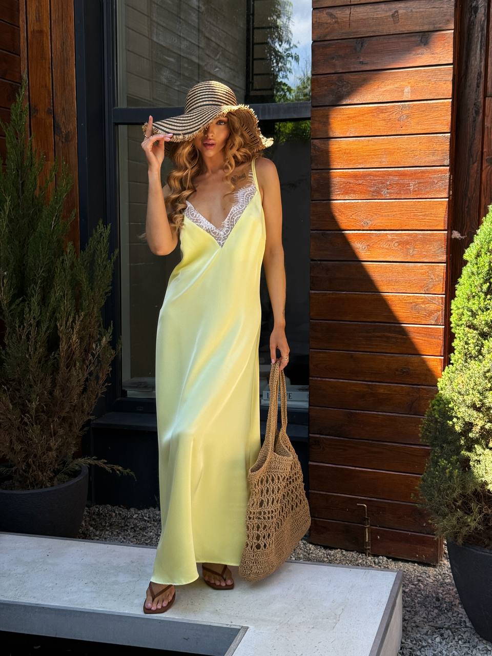Woman in a yellow dress and straw hat standing outside a wooden building.