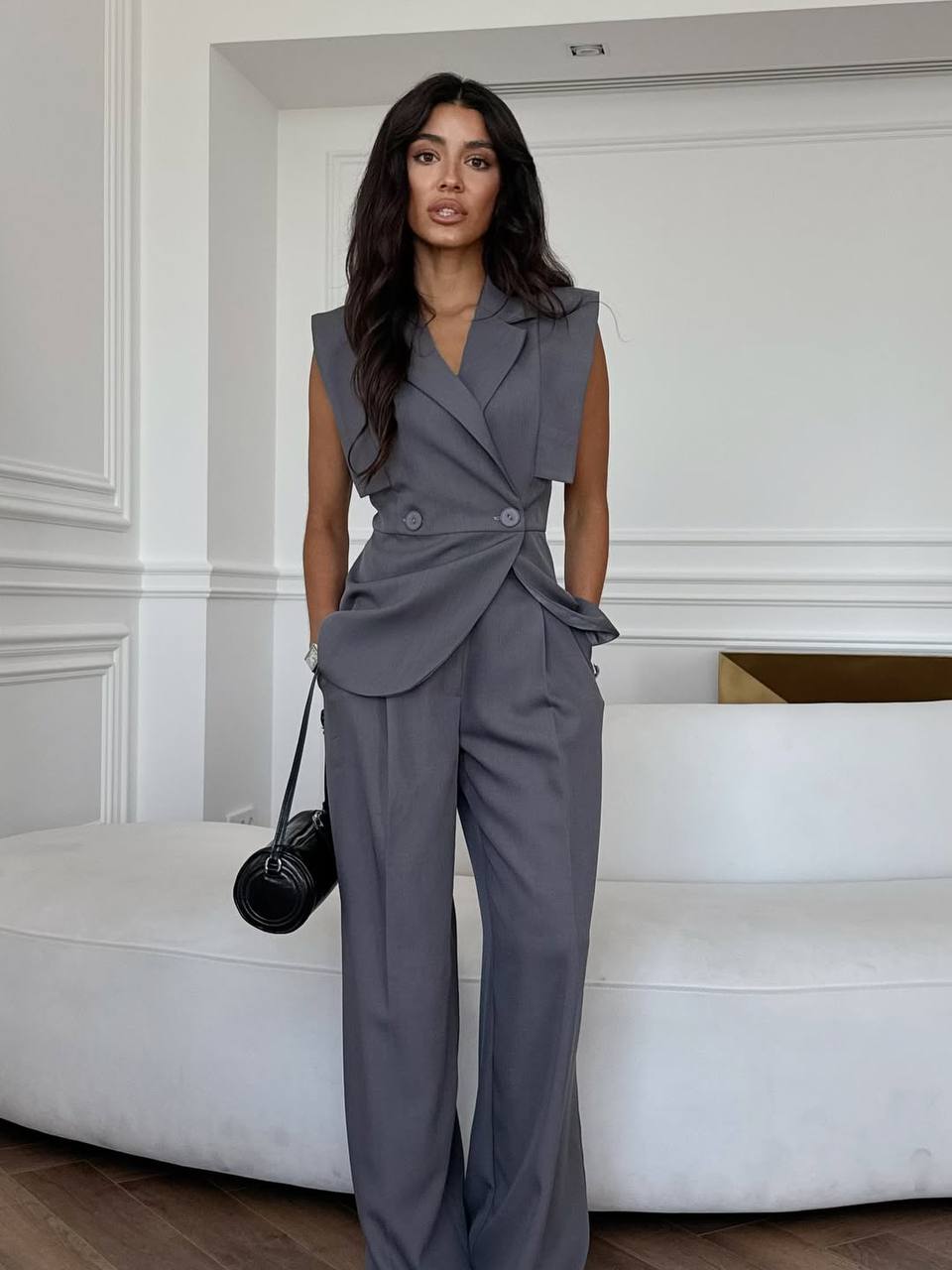 Woman wearing a gray sleeveless top and pants in an elegant room.