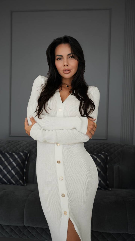 Woman wearing a white dress with a button detail against a gray wall.