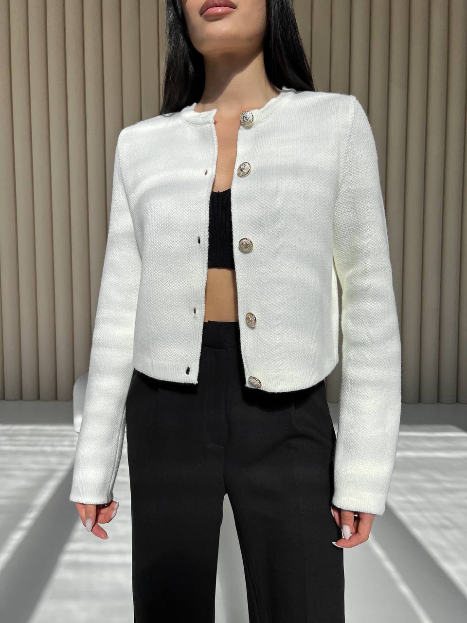 Person wearing a white textured jacket with metallic buttons against a neutral background