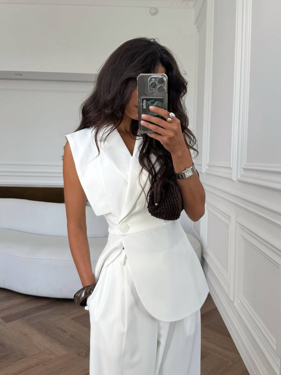Woman taking a mirror selfie wearing a white outfit in a minimalistic room.