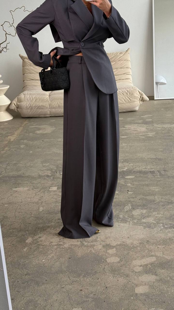 Person wearing a dark gray suit with wide-leg pants in an indoor setting.