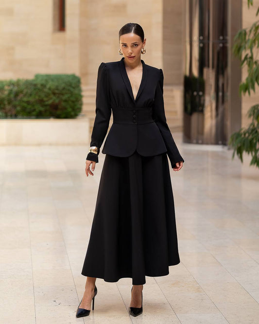 Woman wearing a black suit standing in an elegant indoor setting.