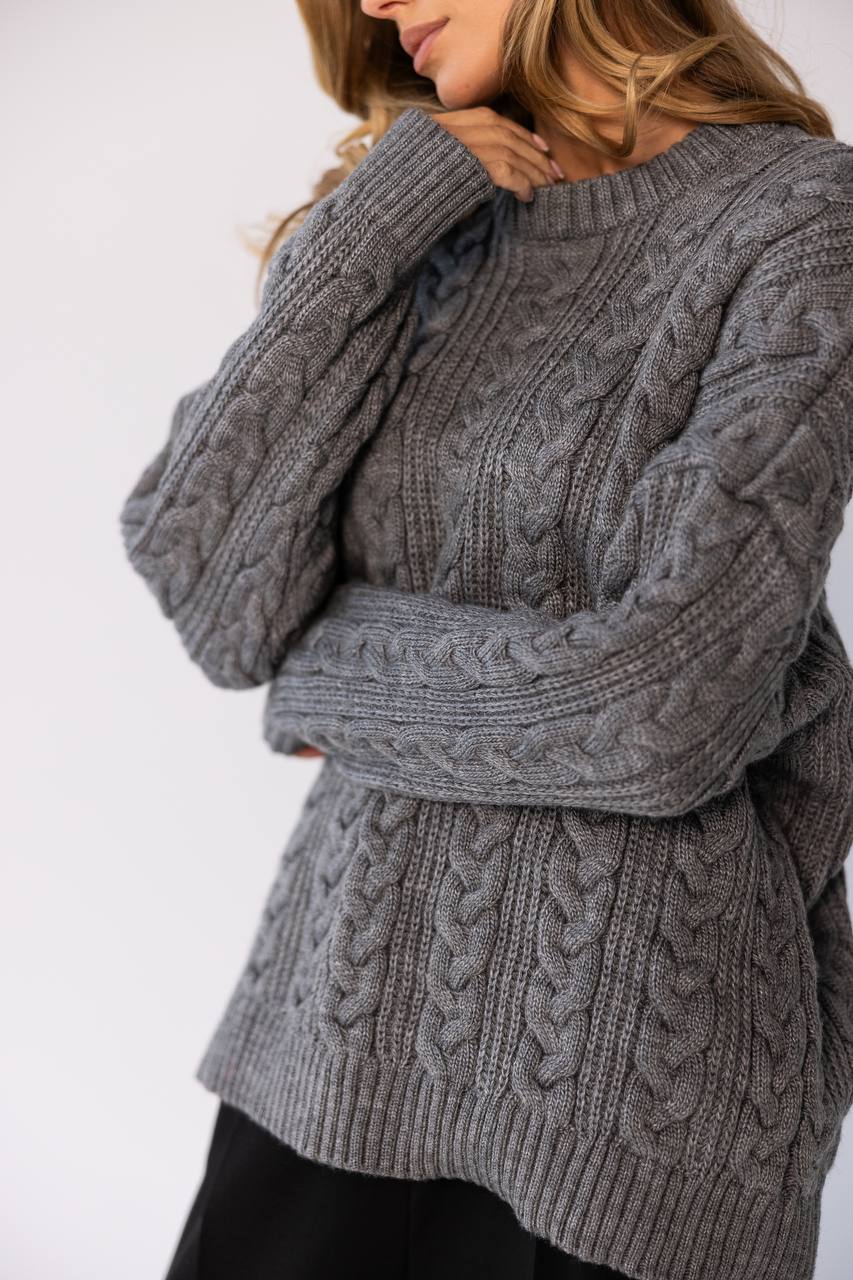 Person wearing a gray cable knit sweater on a white background