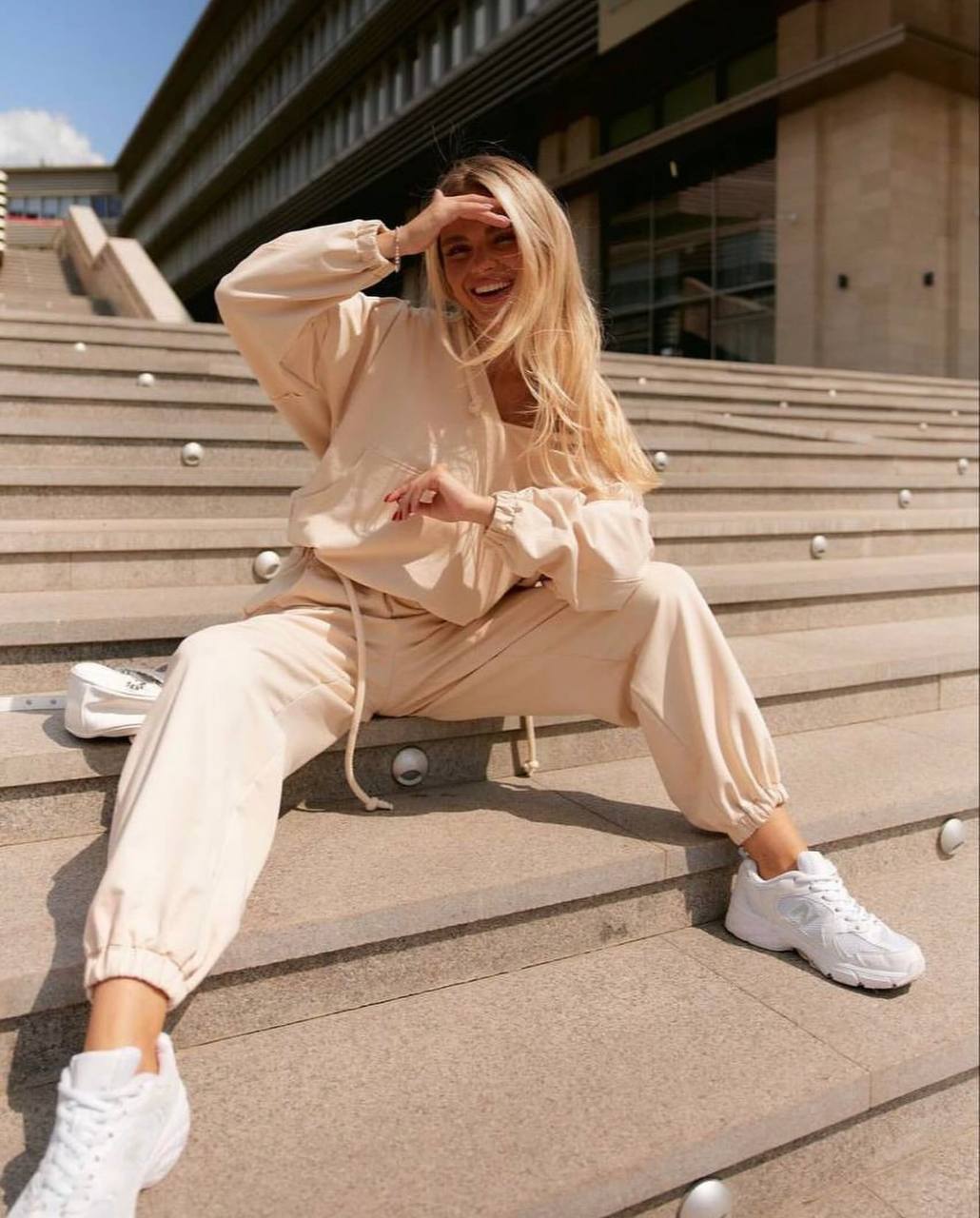 Woman in beige outfit with white sneakers sitting on steps outdoors