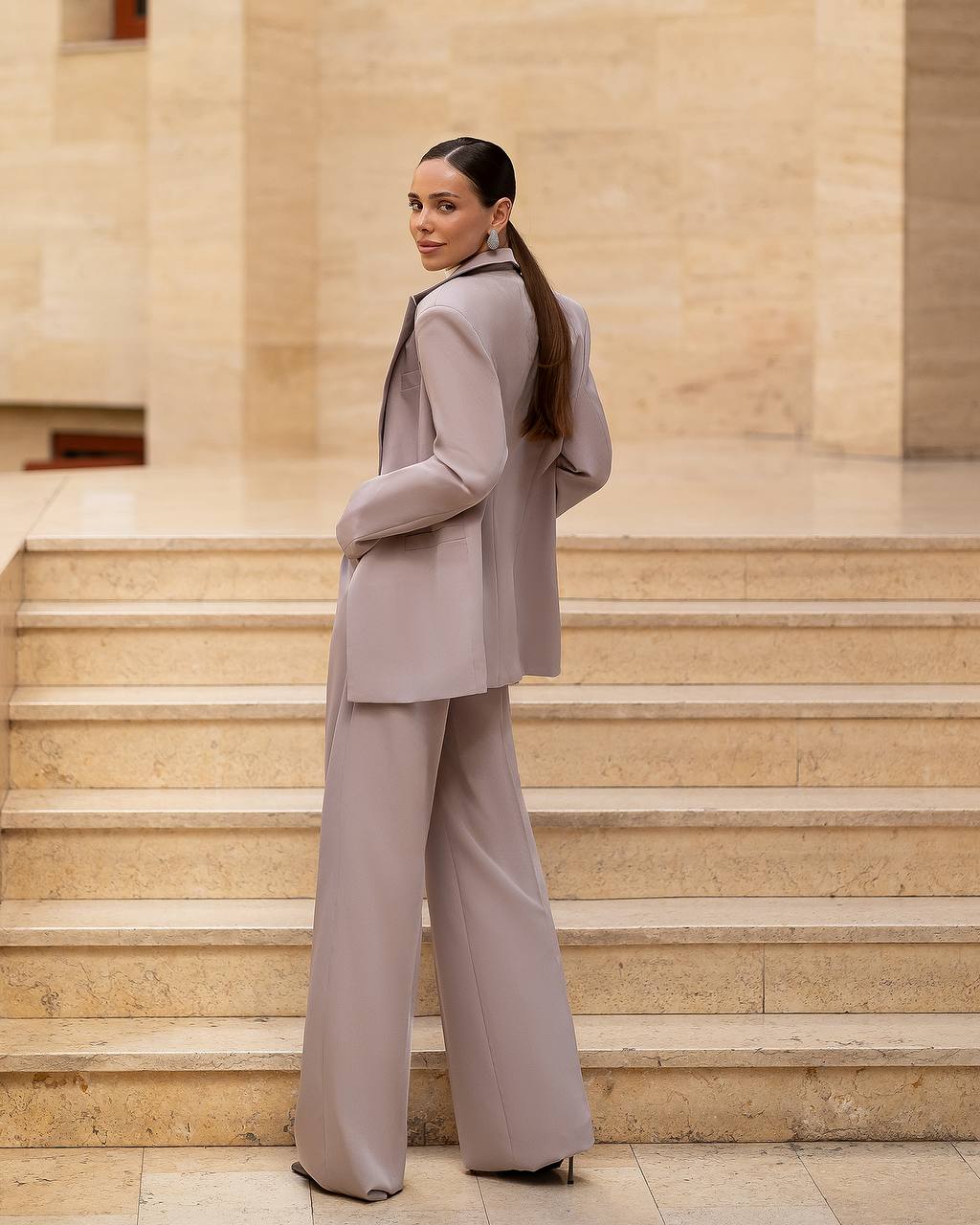 Woman in a gray suit standing on stone steps with a neutral background