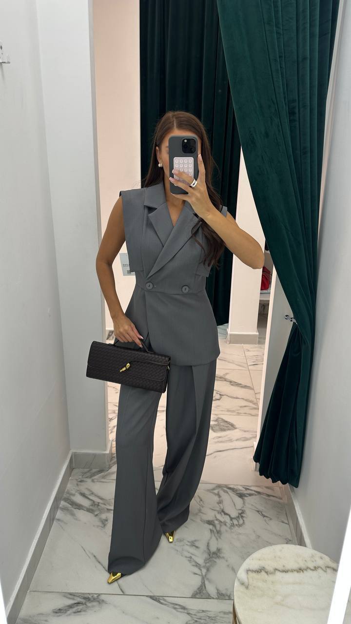 Person wearing a gray suit with a black handbag in a marble-floored room.