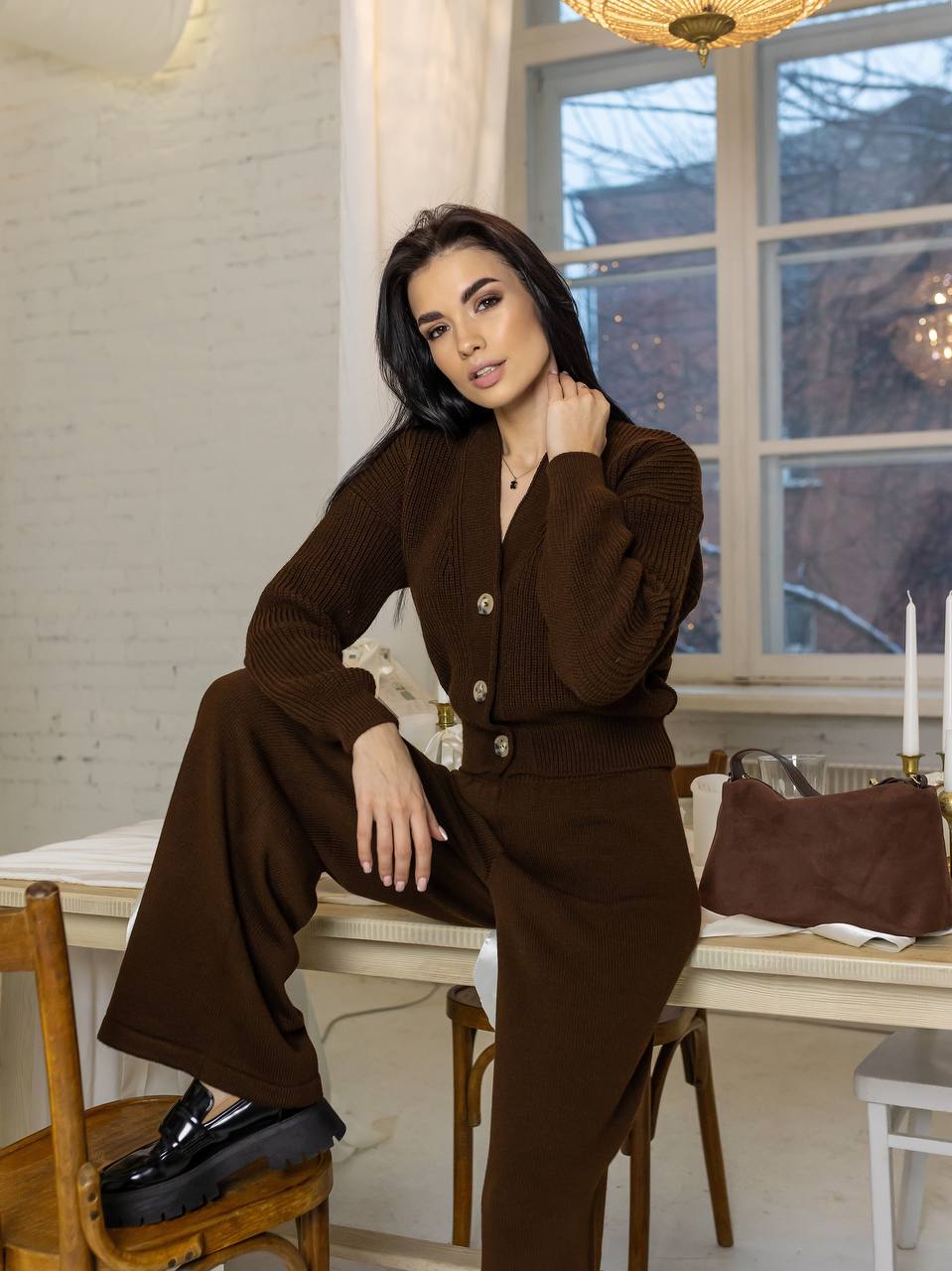 Woman in a brown outfit sitting at a table with a window in the background