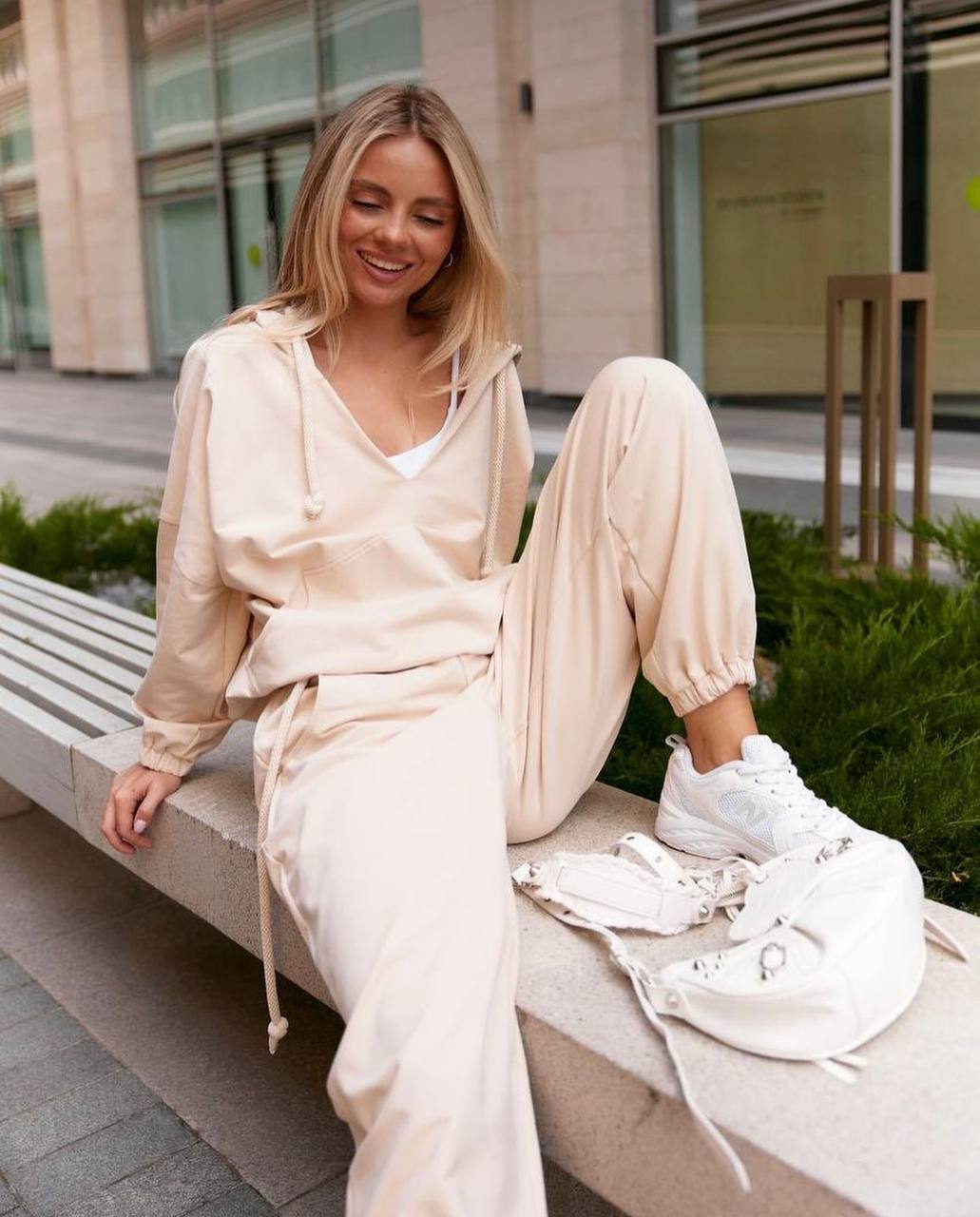 Woman in a beige tracksuit sitting on a bench outdoors