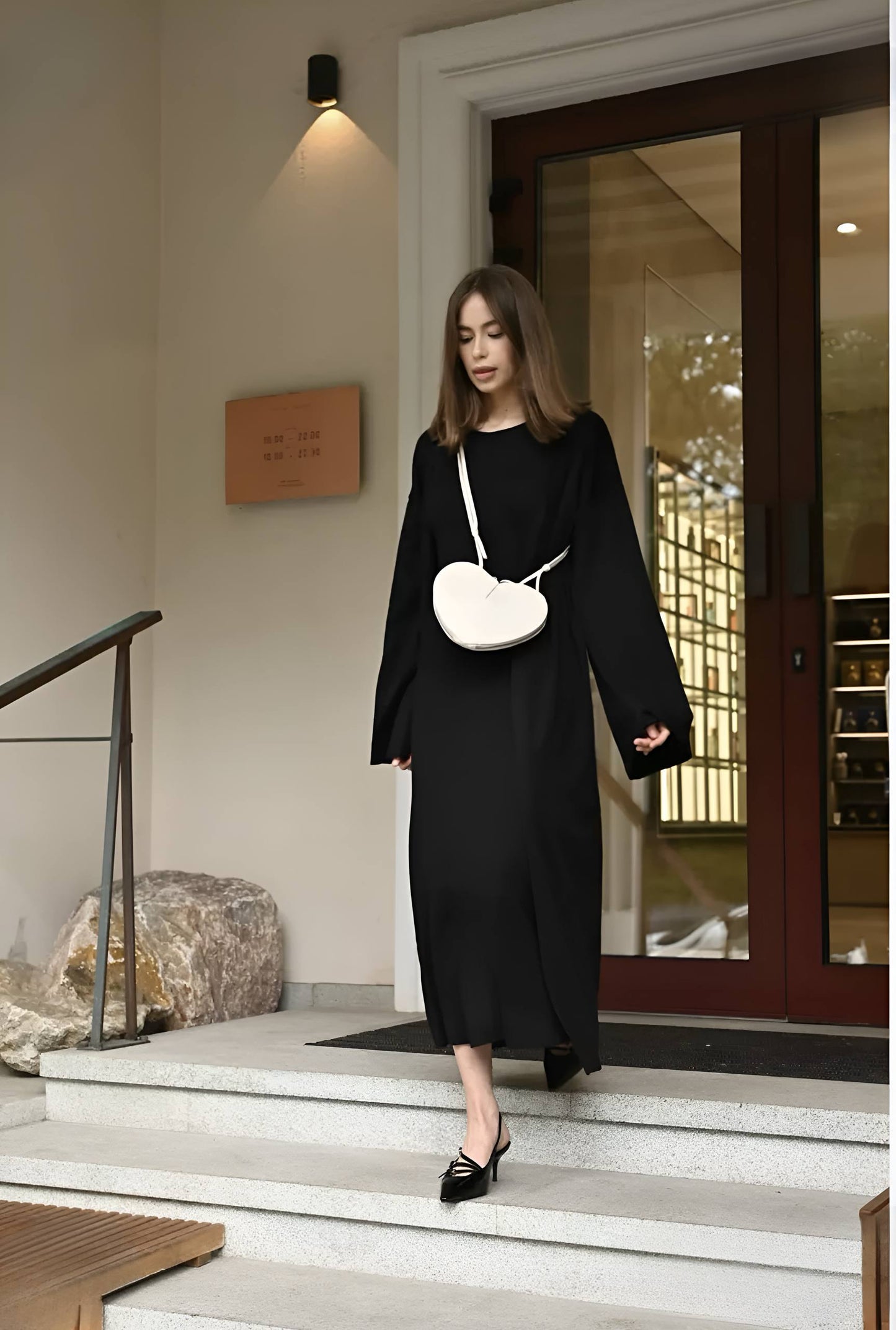 Woman in a black outfit with a white handbag walking out of a building.